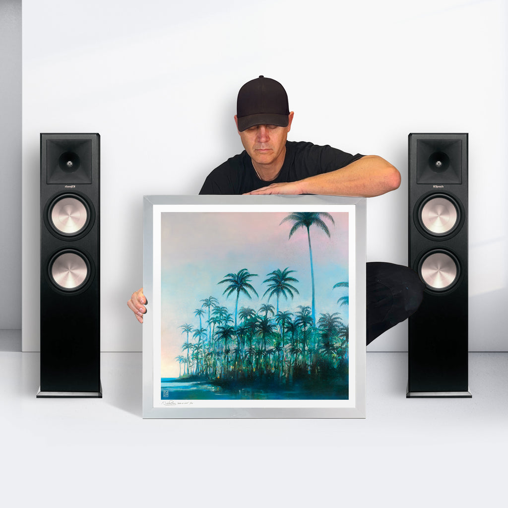 Nick holding a framed Palms print between two speakers, showing the artwork’s scale.